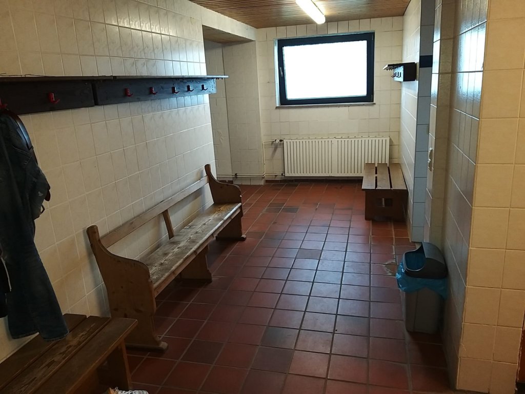 geflieste Umkleide, alte Holzbänke, Leuchtstoffröhre an der Decke.